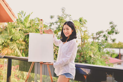 Portrait of woman standing by canvas against sky