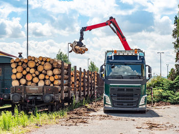 Road truck is loading the railway heavy wagon with spruce trunks. railway depot