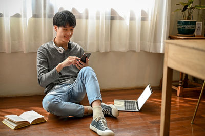 Side view of young man using mobile phone at home