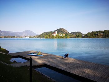 Boy on pier at lake against clear sky