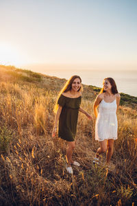 Female friends walking on land against sky during sunset