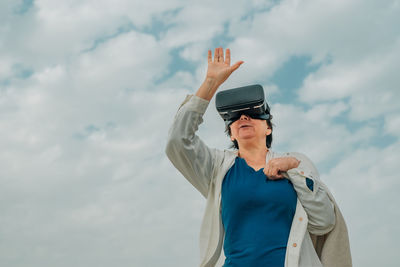 An adult woman against a blue sky with white clouds in vr virtual reality glasses on her eyes