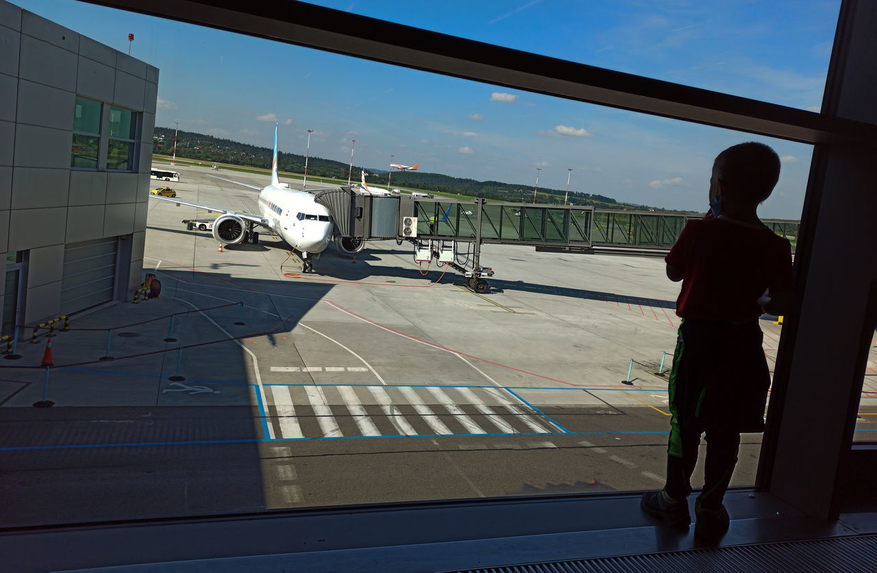 MAN STANDING BY WINDOW AT AIRPORT RUNWAY