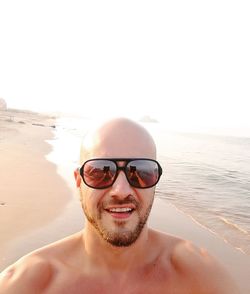 Portrait of young man wearing sunglasses at beach against clear sky