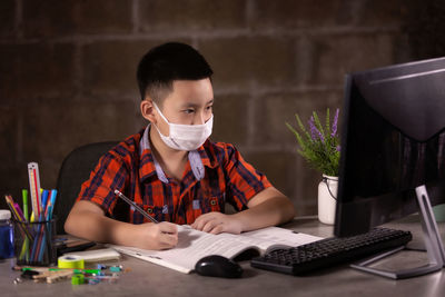 Happy boy studying with face mask on table at home