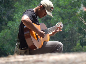 Side view of man sitting with guitar against plants