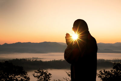 Side view of man praying against sky during sunset