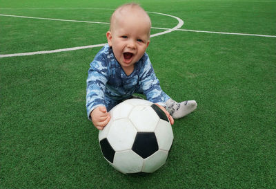 Portrait of cute baby boy with ball siting on soccer field