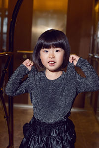 Beautiful korean girl child in a black dress is sitting on a luggage trolley in a hotel