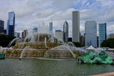 Fountain in city by river against sky