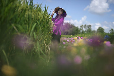 Woman standing on pink flowering plants on field against sky