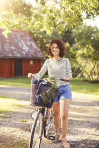 Portrait of smiling woman with bicycle standing at backyard