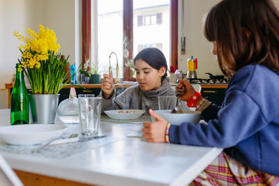 Two children eating lunch at home at white table with yellow flowers