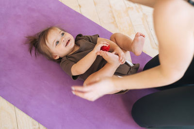Young woman fit mom with baby girl doing exercises with massage ball on mat at the home