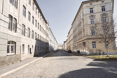 Road by buildings against clear sky in city