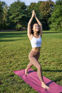 Full length of young woman exercising on field