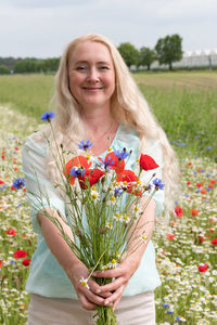 Beautiful middle-aged blonde woman stands among a flowering field of poppies