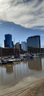 Sailboats moored on sea by buildings in city against sky