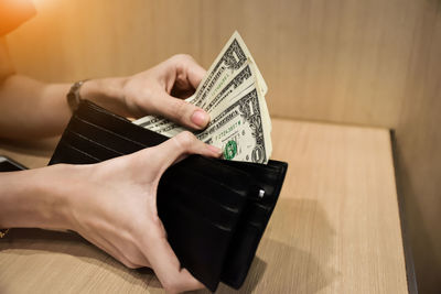 Close-up of woman holding paper currency and wallet over table