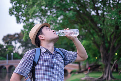 Man drinking water from bottle against tree