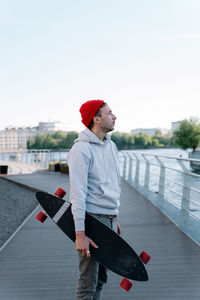 Hipster guy with longboard on city bridge. trendy man hipster skateboarder hold skateboard in hand