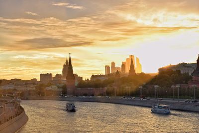 Boats in moskva river by spasskaya tower against cloudy sky during sunset
