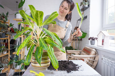 Portrait of young woman standing by potted plant