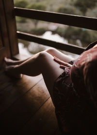Lower section of woman sitting on ledge of wooden cabin at sunset