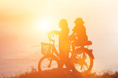 People riding bicycle against sky during sunset