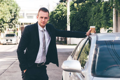 Portrait of businessman standing with car on road