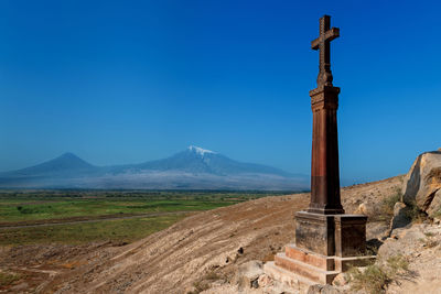 Cross on land against mountain range against clear blue sky