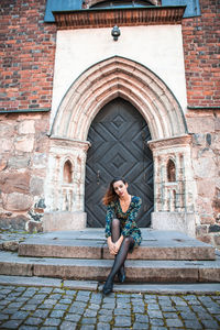 Full length portrait of woman sitting against brick wall