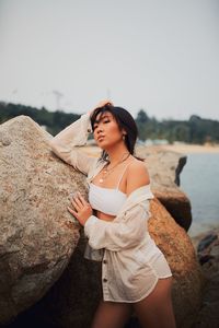Young woman standing on rock against sky