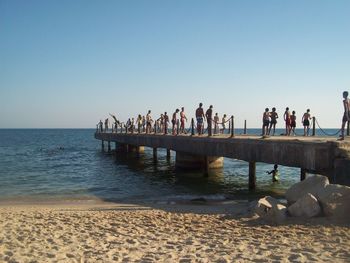 People on pier over sea against clear sky