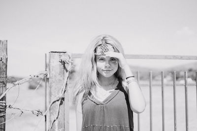 Portrait of smiling woman shielding eyes while standing by fence