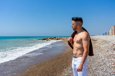 Man standing at beach against clear blue sky