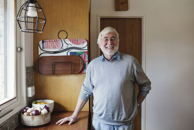 Portrait of smiling senior man standing by kitchen counter at home