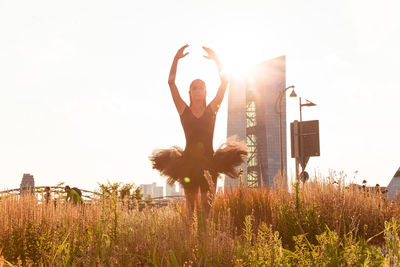 Ballet dancer dancing amidst plants on field against clear sky