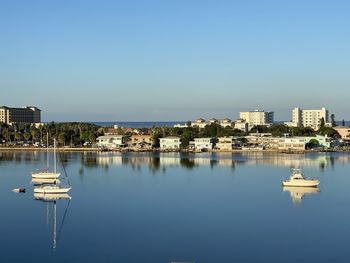 Sailboats in city by lake against clear blue sky