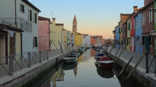 Boats moored in canal by buildings against sky