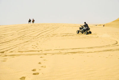 Man riding motorcycle on desert against clear sky