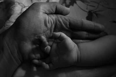 Cropped hands of parent and baby on bed at home