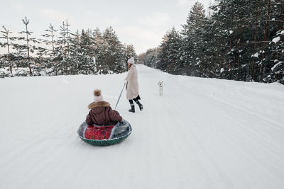 Mother sleds her daughter in a snowy forest