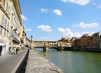 Bridge over river by buildings in town against sky