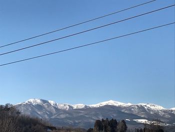 Low angle view of snowcapped mountains against clear blue sky