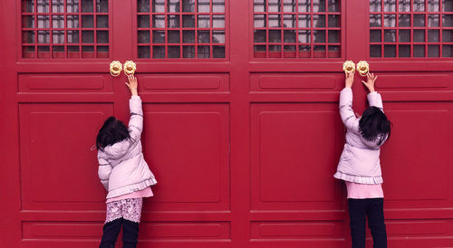 Rear view of girls reaching knobs of red doors