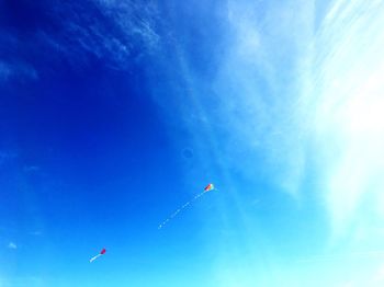 Low angle view of kites flying against blue sky