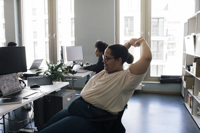 Female business professional stretching while sitting on chair at office