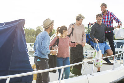 Happy friends boarding yacht against sky