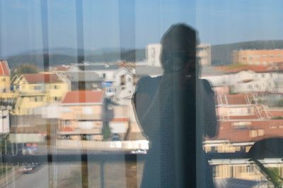 Woman standing in city against sky seen through window